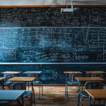 Salle de classe avec un grand tableau noir rempli de formules et de schémas scientifiques, entourée de bureaux vides